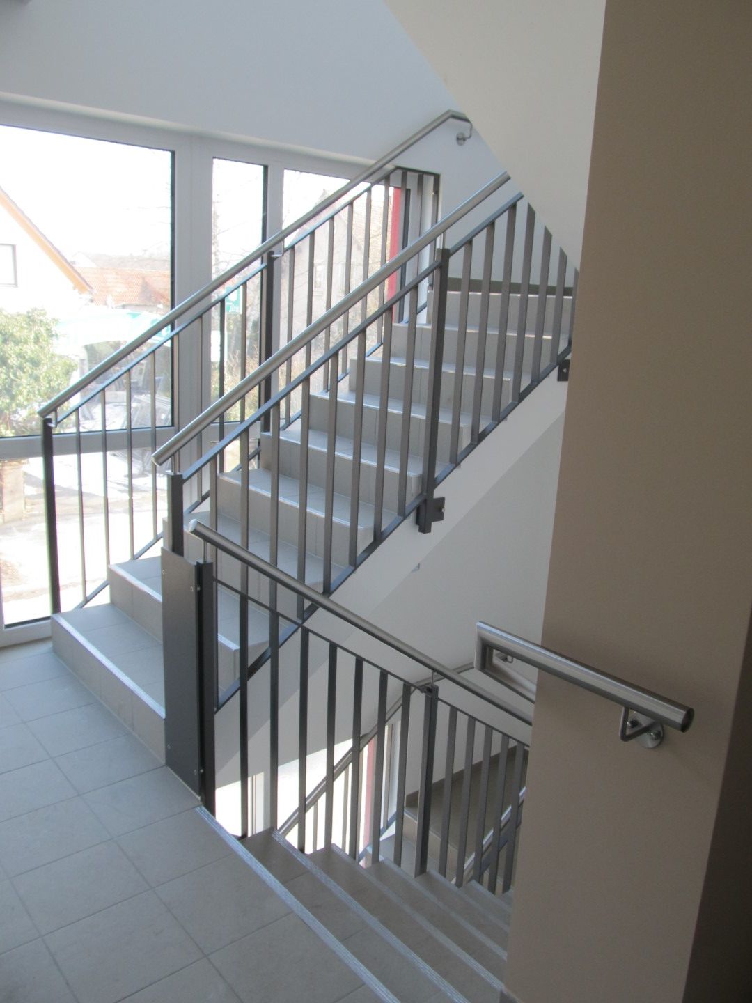 Treppe mit Metallgeländer; durch eine Glastür auf der linken Seite strömt Sonnenlicht herein.