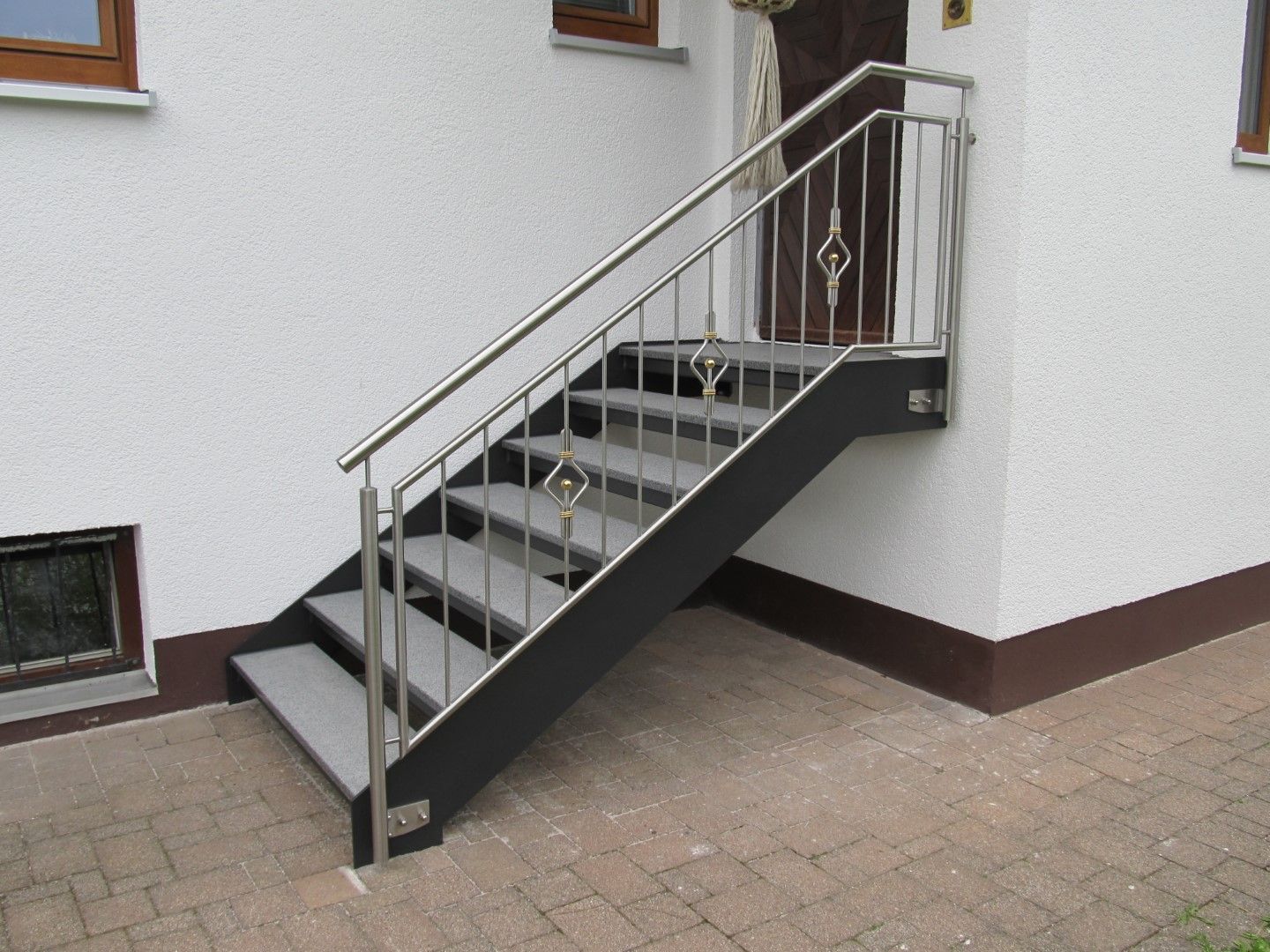 Graue Außentreppe mit Metallhandläufen, die zu einer Eingangstür vor einem weißen Gebäude führt.