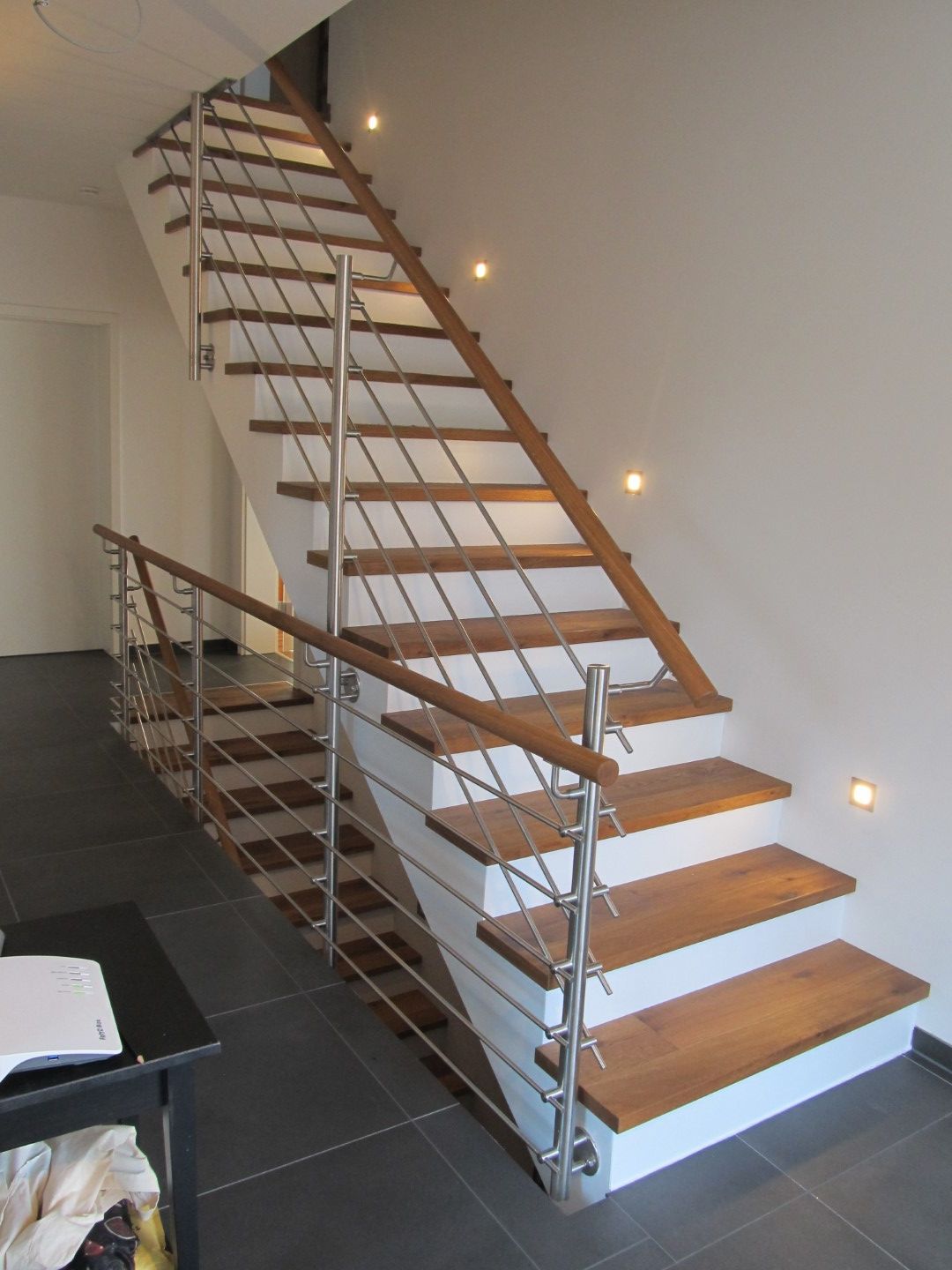 Holztreppe mit Metallgeländer und eingebauter Beleuchtung. Weiße Wand, dunkler Boden.