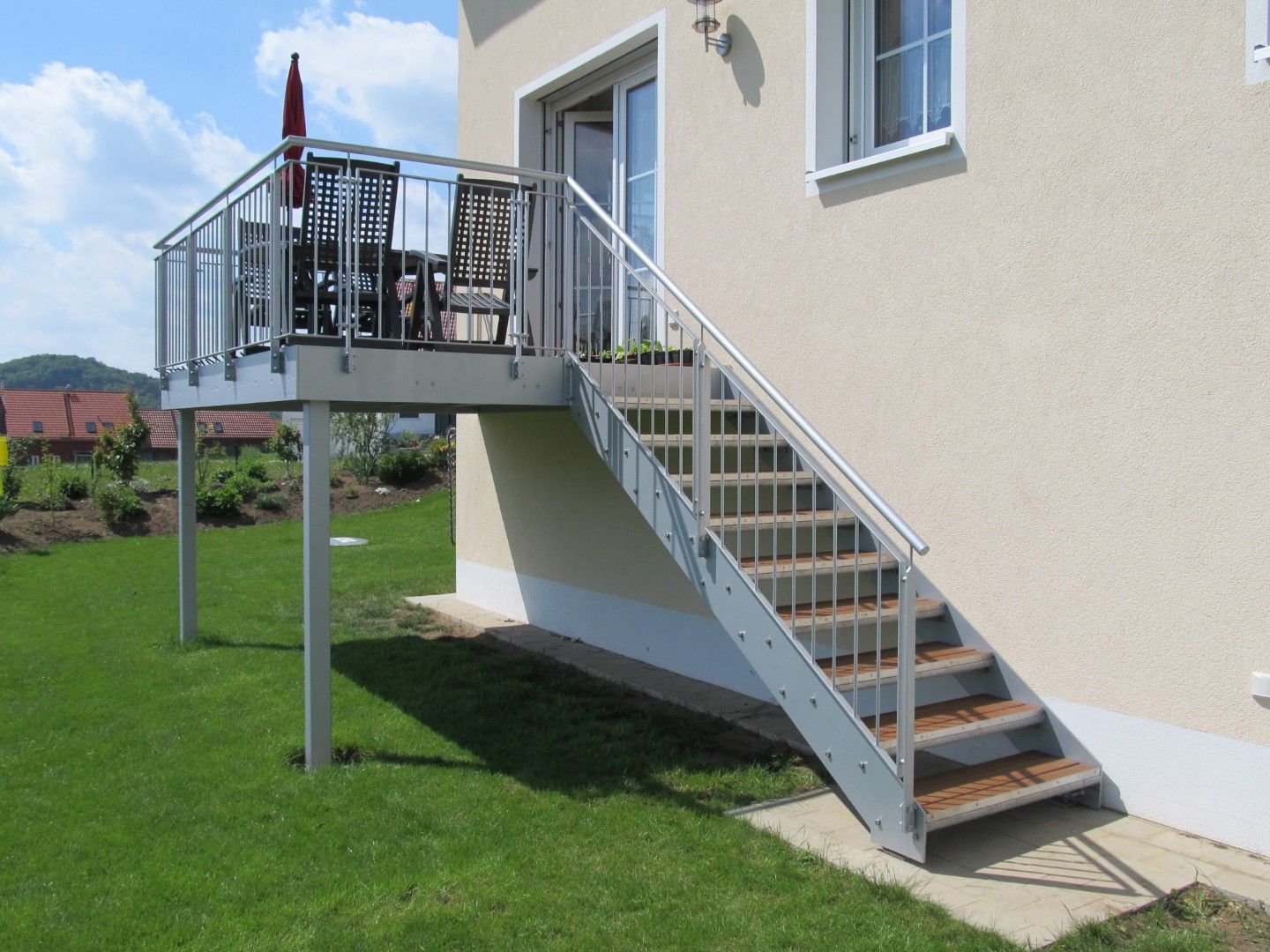 Metalltreppe, die zu einer kleinen Terrasse außerhalb eines zweistöckigen Hauses auf einer Rasenfläche führt.