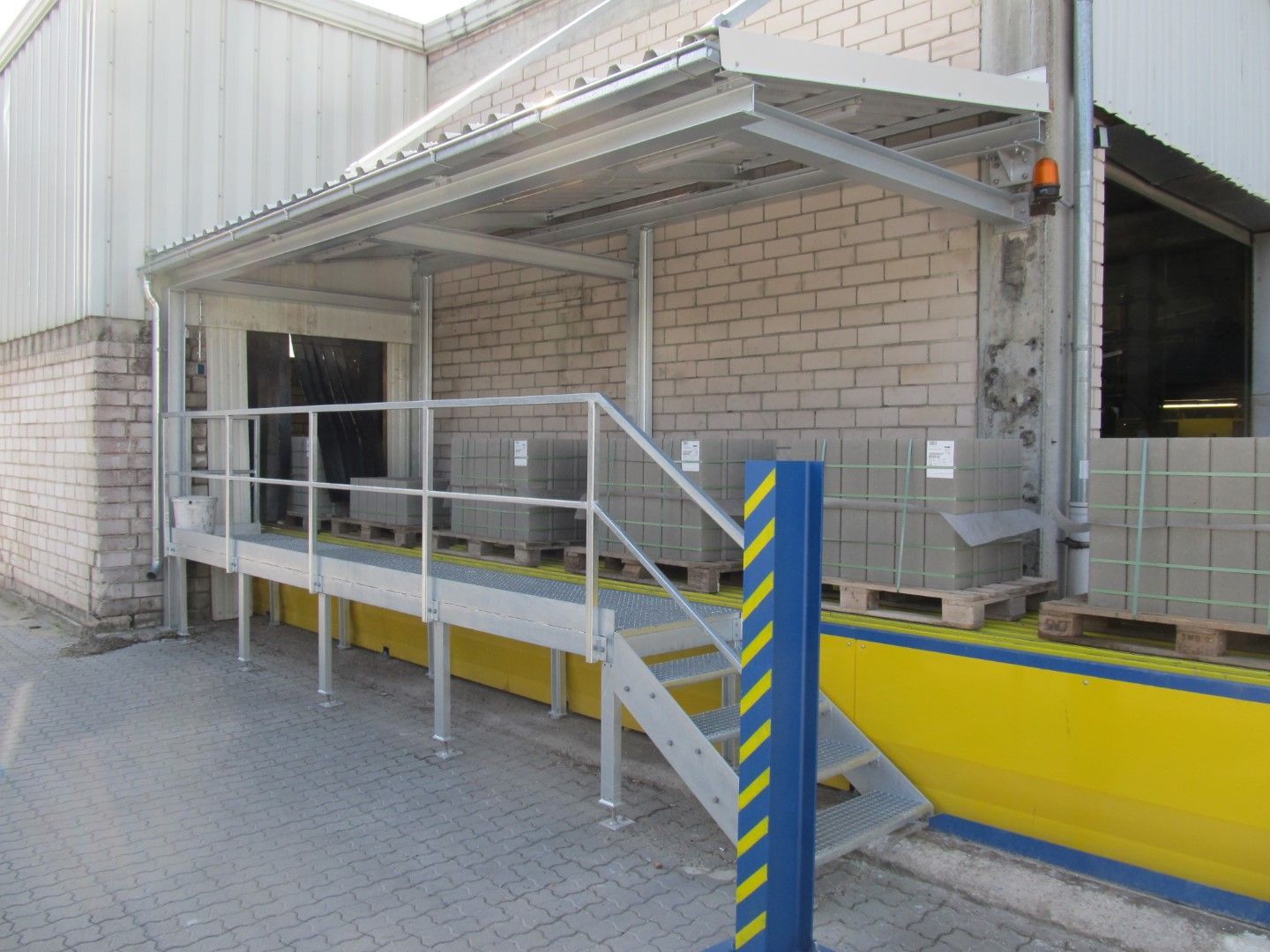 Laderampe mit Rampe und Handläufen. Ziegelwand, Metallstützen, gelbe Sicherheitsakzente.