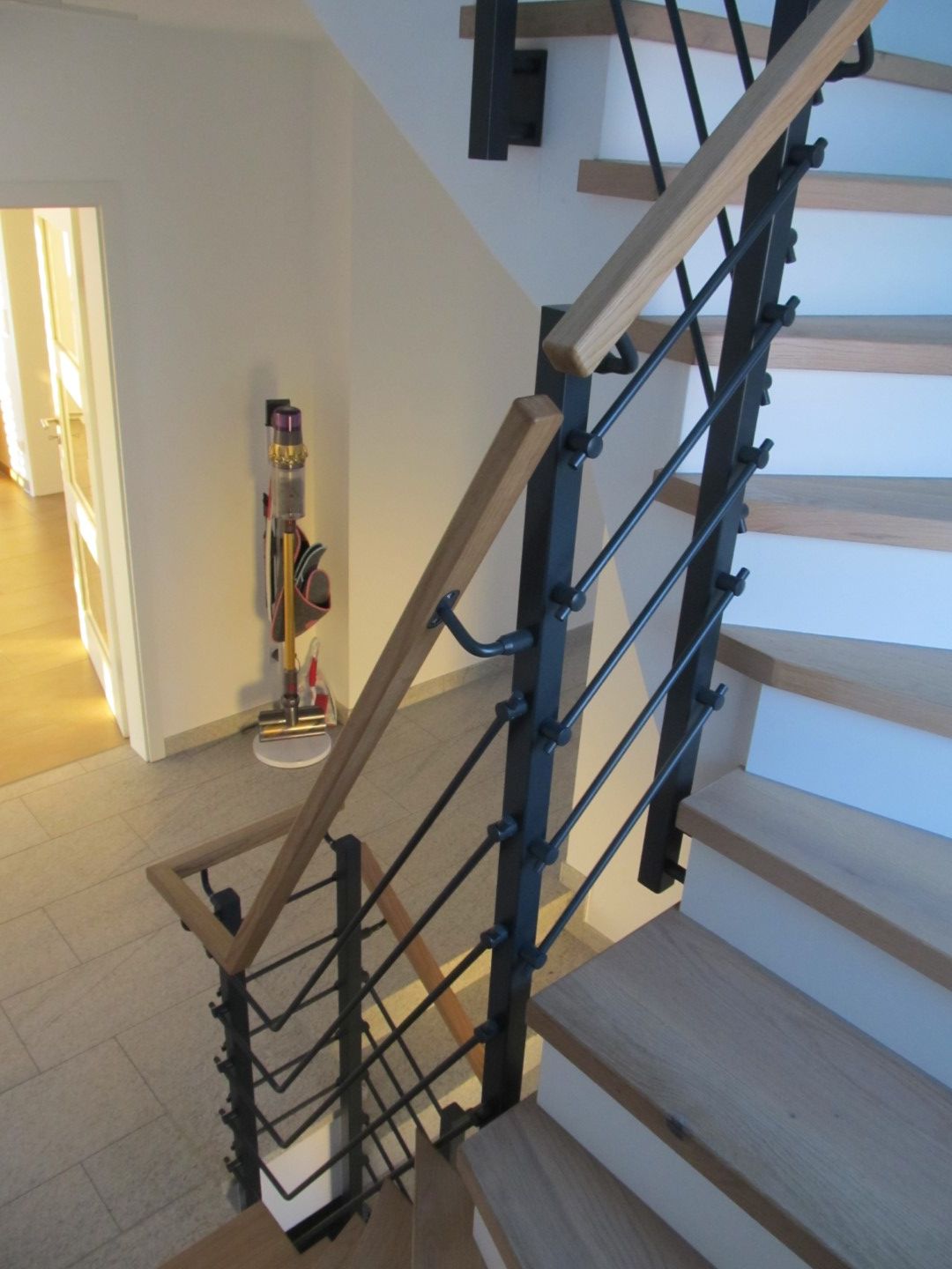 Treppe mit Holzstufen und Handlauf, schwarzen Metallstangen und hellem Holz.