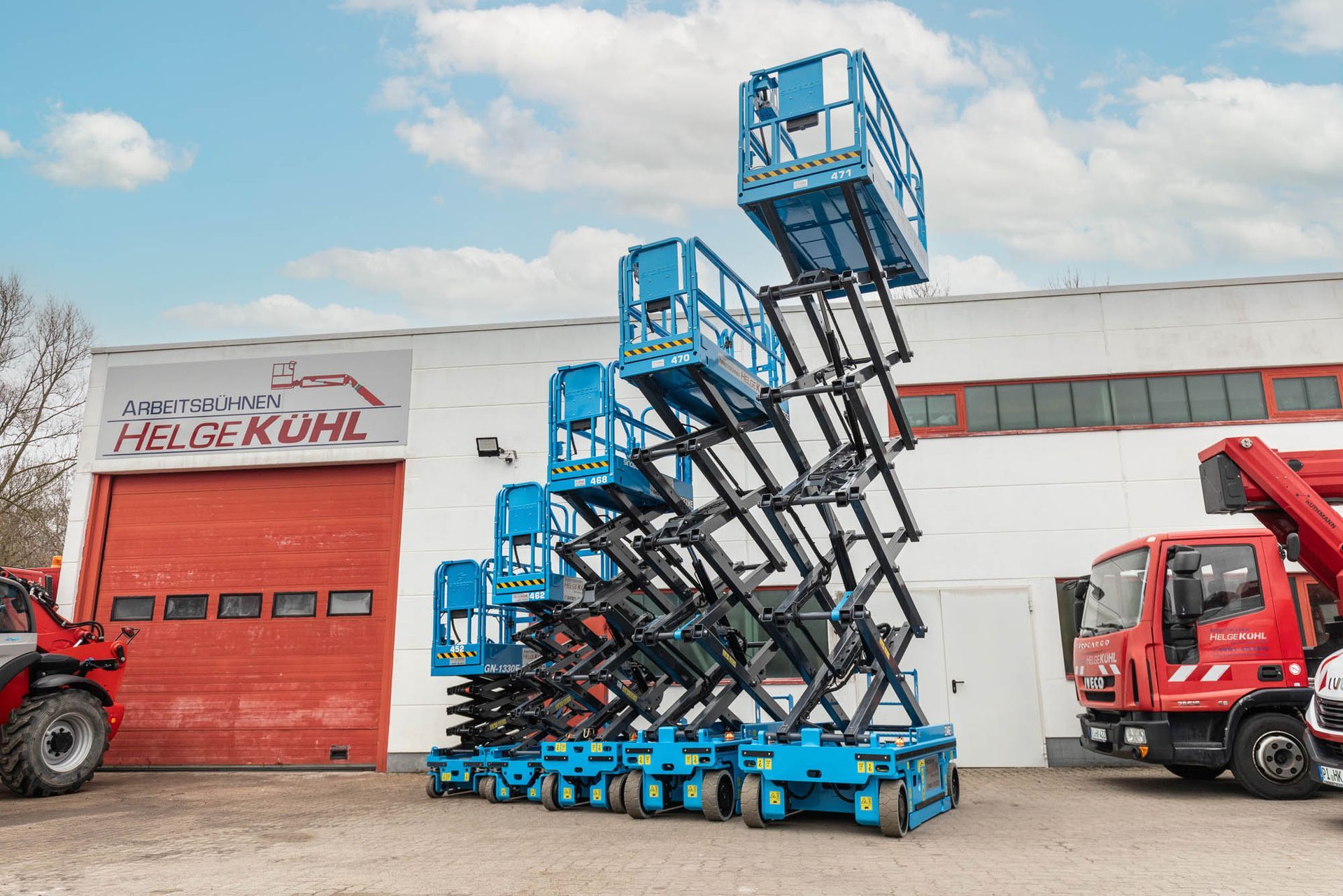 Vor einem Gebäude ist eine Reihe von Scherenhebebühnen übereinander gestapelt.