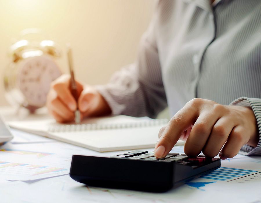 Una mujer está usando una calculadora mientras escribe en un cuaderno.