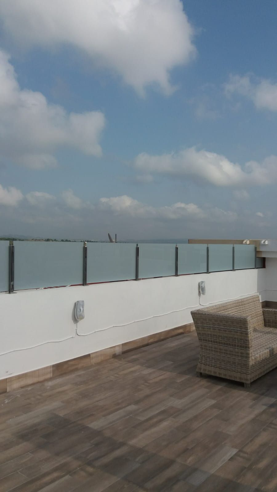 Un balcón con una silla de mimbre y una barandilla de cristal.