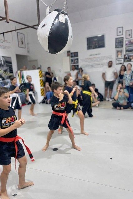 Niños practicando artes marciales en un estudio, pateando un saco de entrenamiento colgado.