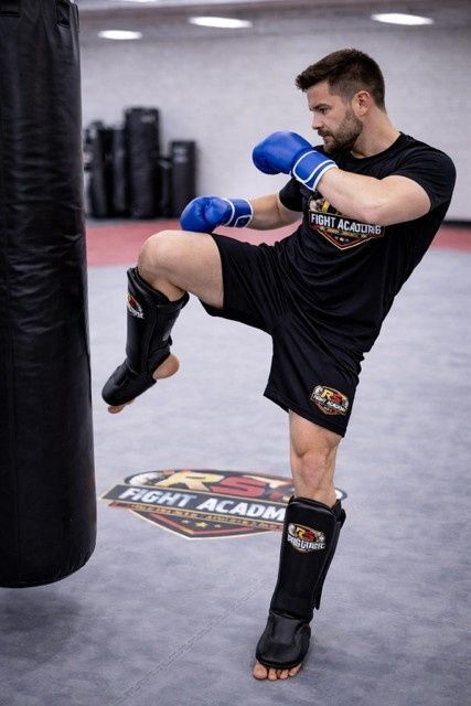 Hombre con guantes azules practicando rodillazos en un saco de boxeo en un gimnasio.