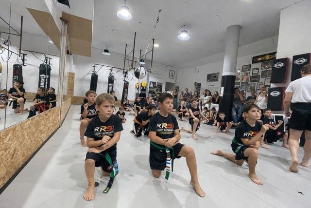 Niños practicando estocadas de artes marciales en un estudio luminoso con espejos y sacos de boxeo.