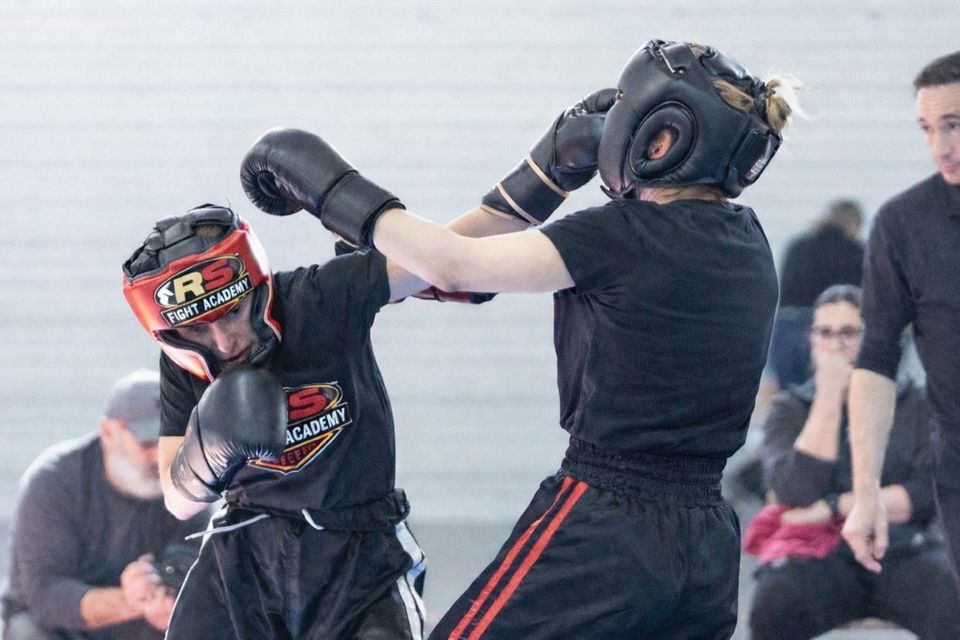 Dos personas practicando boxeo con equipo de entrenamiento en interiores; una lanza un puñetazo 