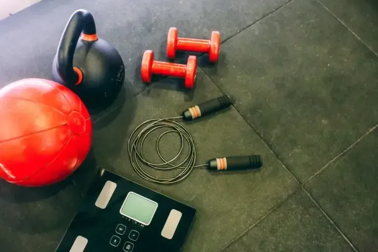 Equipamiento de fitness en el gimnasio: balón medicinal rojo, pesa rusa, mancuernas, cuerda para saltar y báscula.
