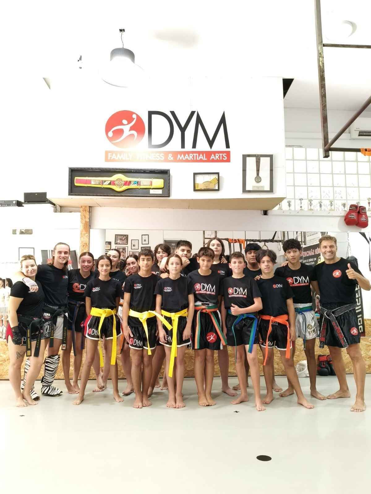 Grupo de estudiantes de artes marciales posando en interiores con uniformes negros y cinturones de colores 