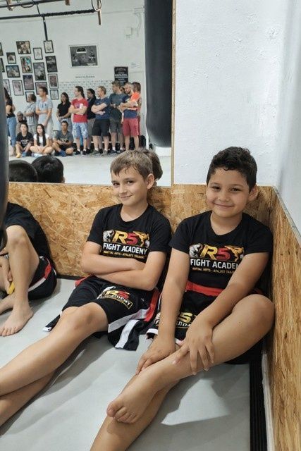 Dos niños sentados en un sofá, sonriendo, con un grupo de personas al fondo.