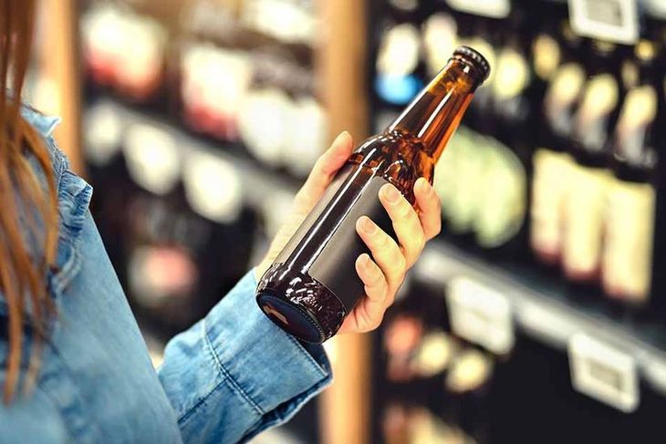 Eine Frau betrachtet eine Bierflasche beim Getränkehändler