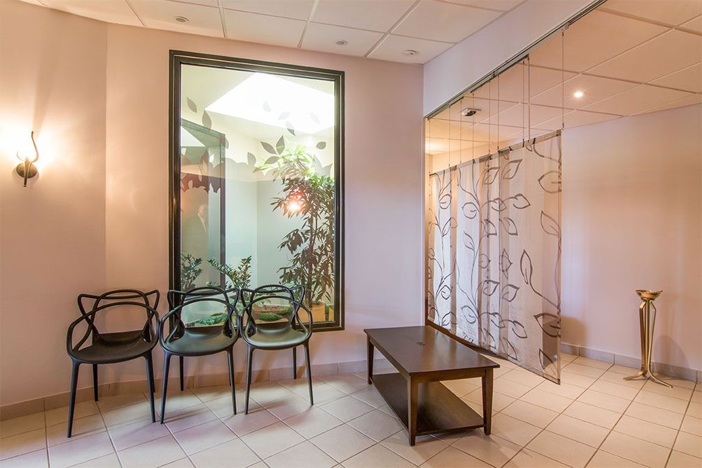 Salle d'attente avec chaises, table, grande fenêtre et porte à rideaux.