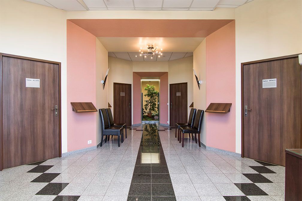 Couloir avec portes, chaises et plante. Murs roses, portes marron, sol carrelé.