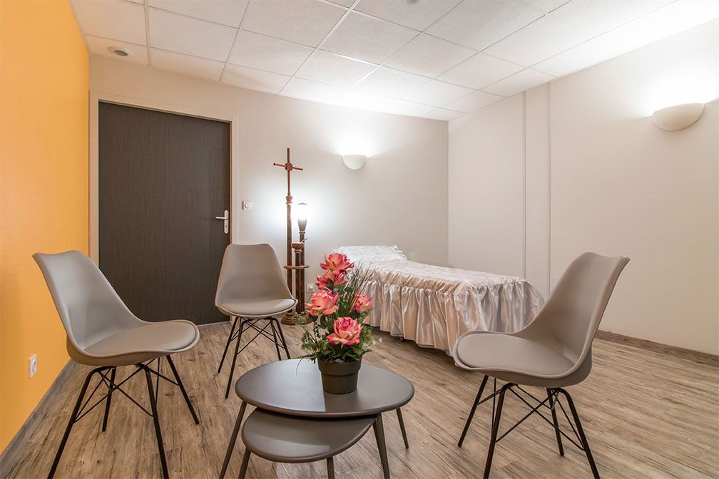 Chambre avec lit, chaises autour d'une petite table, mur orange, parquet.