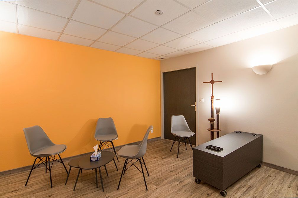 Salle d'attente avec chaises grises, murs orange et beige, porte marron foncé et sol marron.