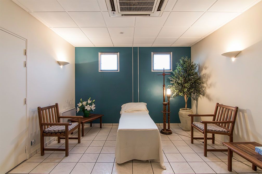 Salle funéraire avec une table recouverte d'un linceul, des chaises et un arbre artificiel.