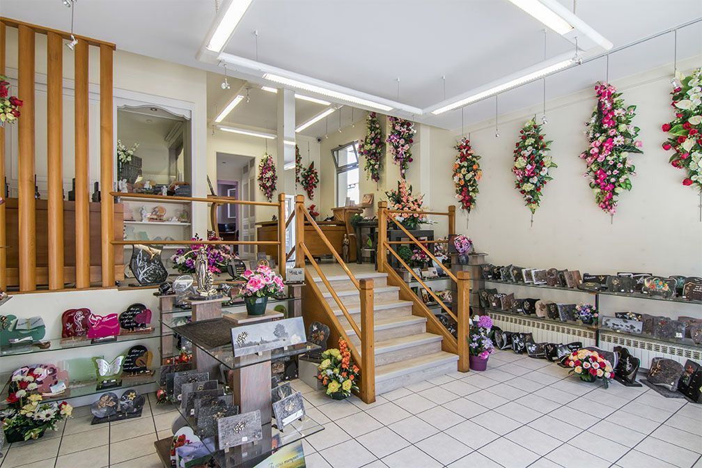 Intérieur d'une boutique de fleurs avec escalier, fleurs décoratives et présentoirs d'objets commémoratifs.