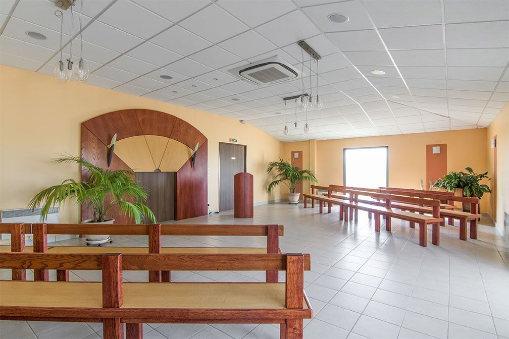 Intérieur d'une salle d'attente avec des bancs en bois, des plantes et un motif en bois en forme d'arche sur le mur.