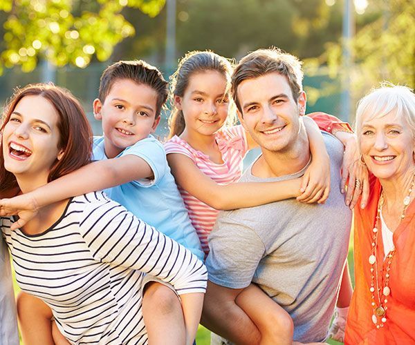Une famille souriante et s'enlaçant à l'extérieur, au soleil.