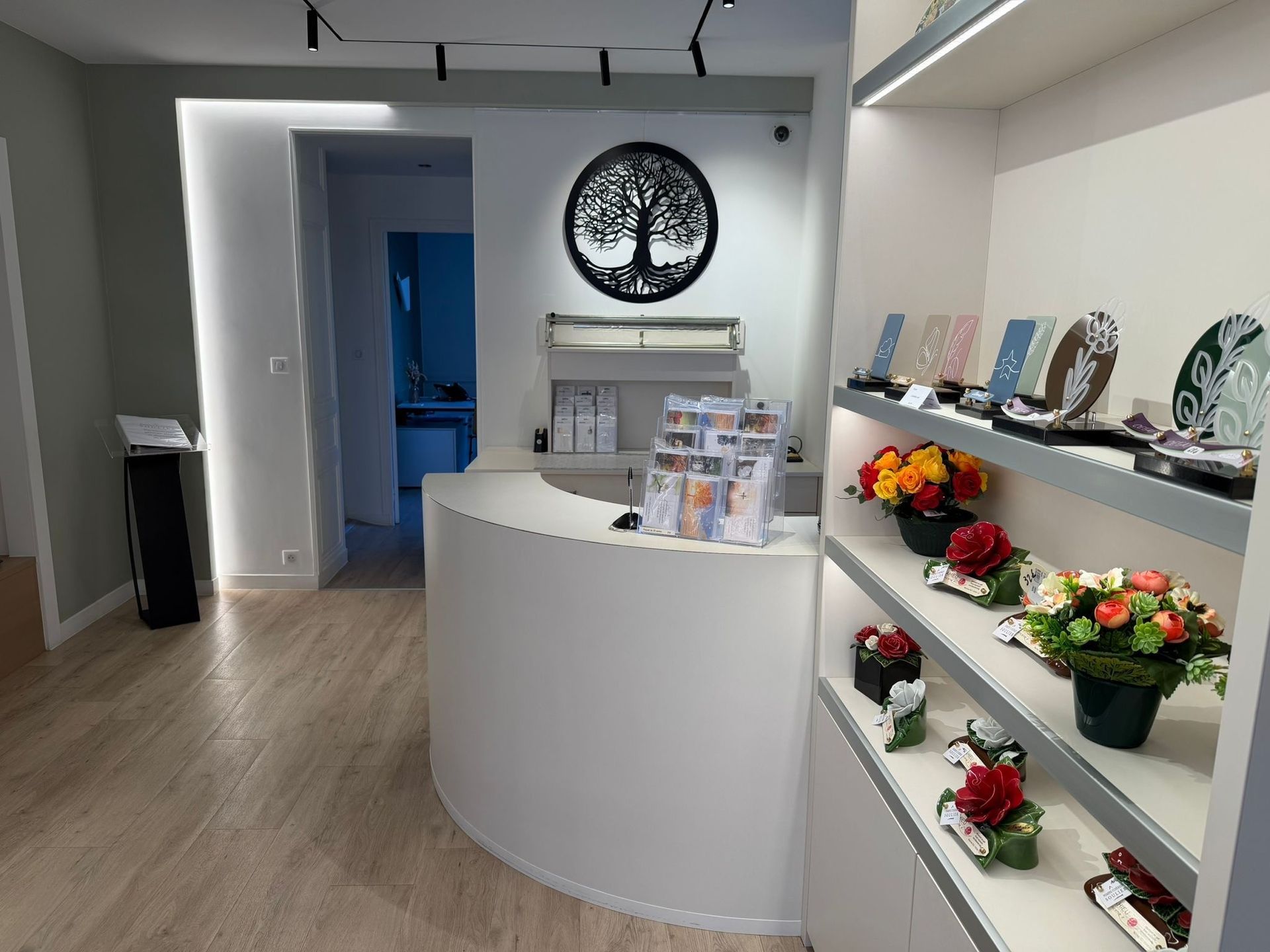 Intérieur d'une maison funéraire avec un bureau en bois, des compositions florales au mur et un petit coin salon.