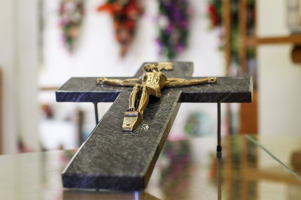 Statue de crucifix avec une figure dorée sur une croix de granit, posée sur une surface réfléchissante, dans une pièce.