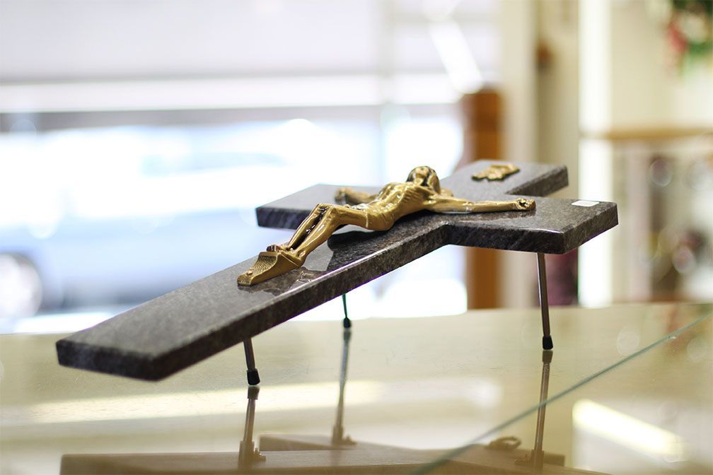 Un Jésus doré sur une croix de pierre gris foncé, soutenue par de fins pieds en métal, sur une surface en verre.