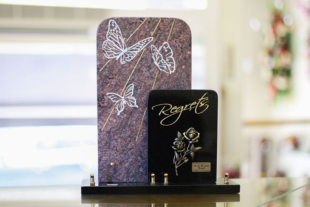 Deux pierres tombales commémoratives ; l'une ornée de papillons et l'autre d'une rose, sur un socle noir.