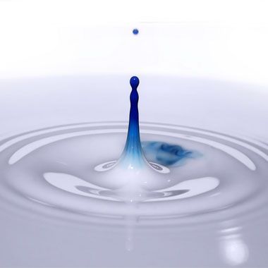 Goutte d'eau bleue suspendue au-dessus d'une piscine à ondulations concentriques.