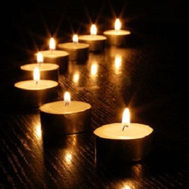 Des bougies chauffe-plat allumées, disposées sur une surface sombre, diffusent une lumière chaude.