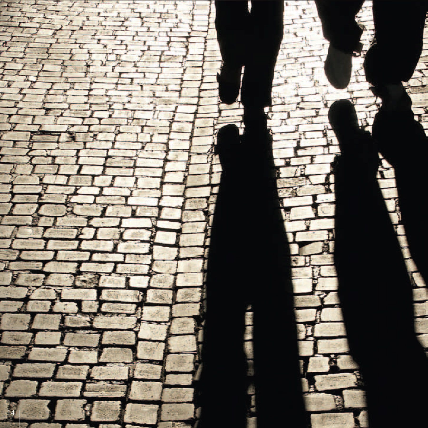 Des jambes et de longues ombres se dessinent sur une surface pavée de briques.