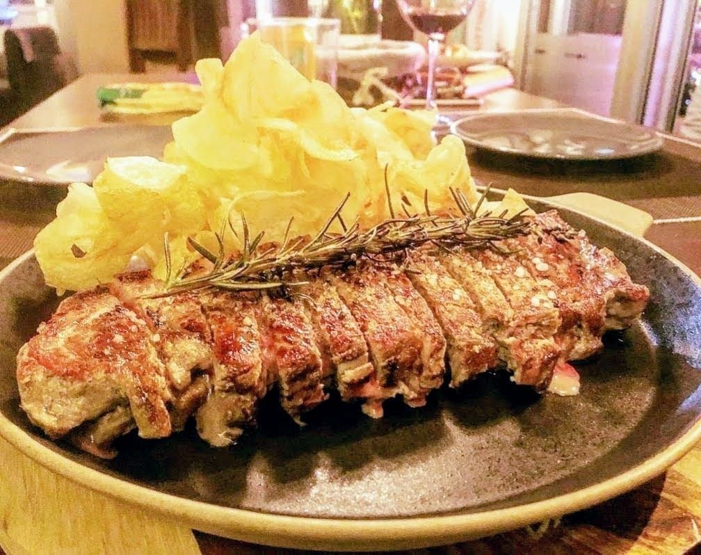 Un trozo grande de carne y patatas fritas en un plato sobre una mesa.