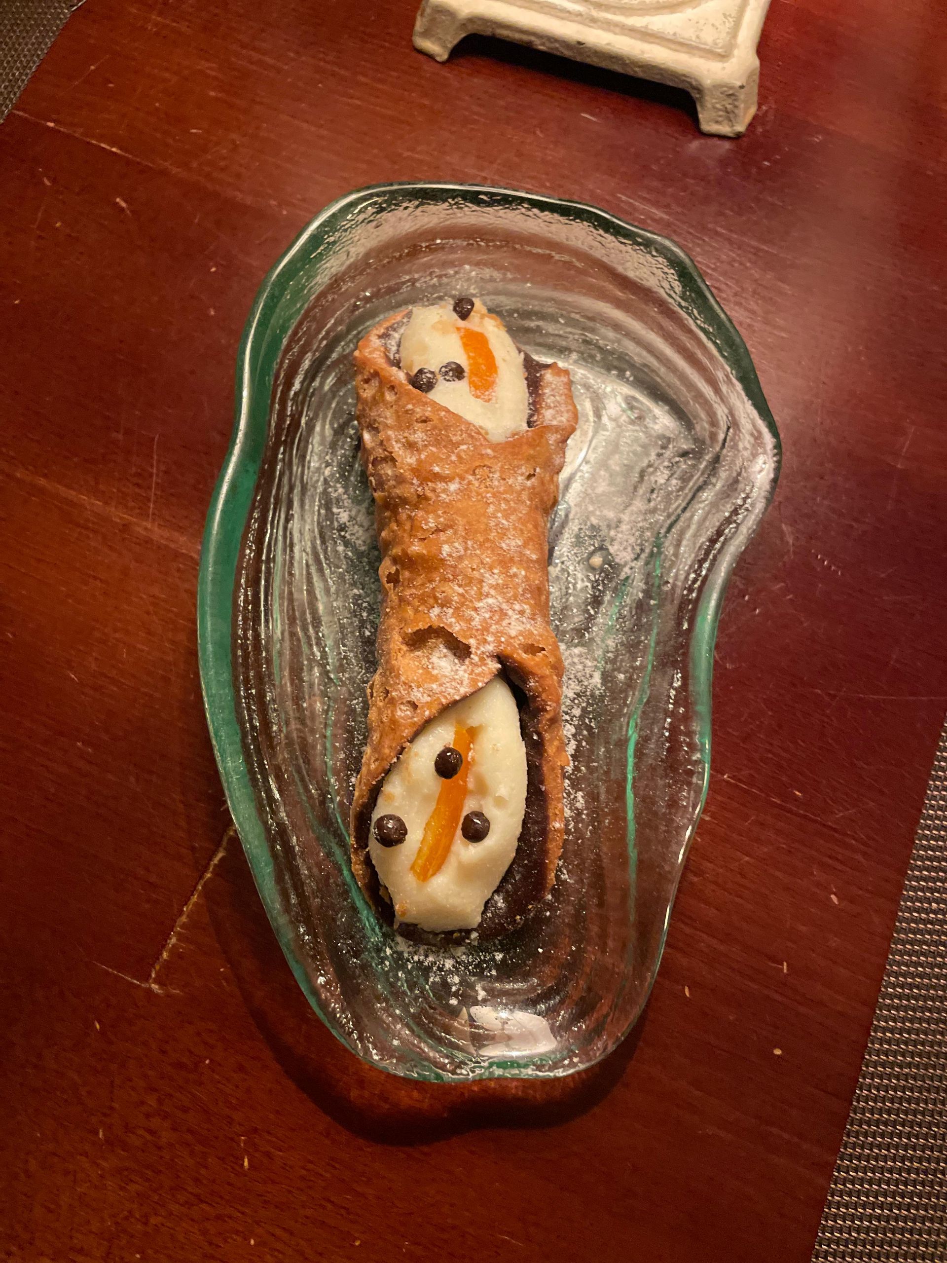 Un cannoli está sentado en un plato de vidrio sobre una mesa.