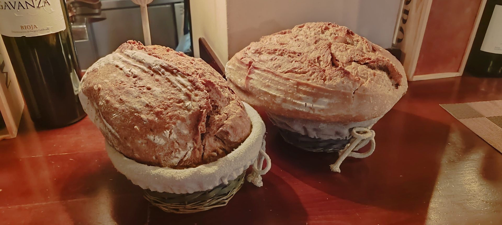 Dos cestas de pan están sobre una mesa de madera junto a una botella de vino.