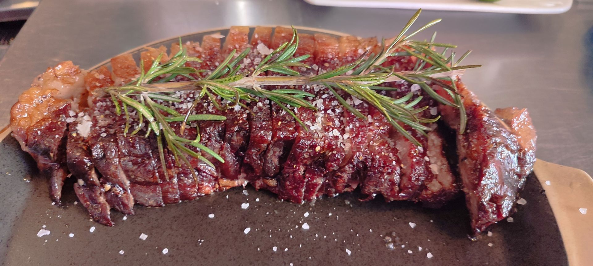 Un trozo de carne con romero encima está en un plato sobre una mesa.
