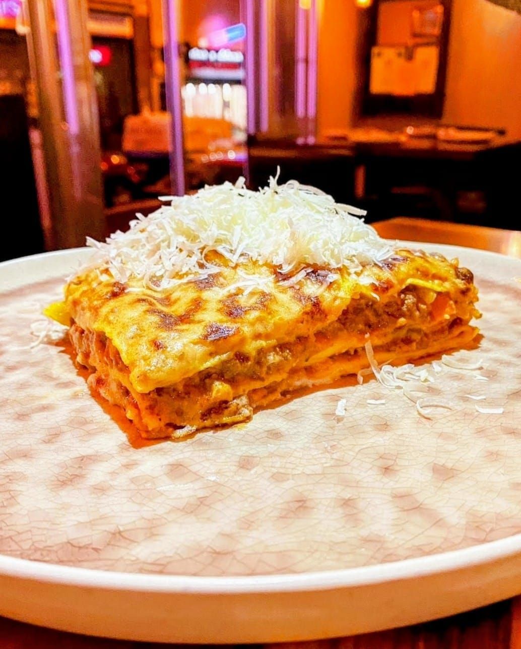 En un plato hay una rebanada de lasaña con queso encima.