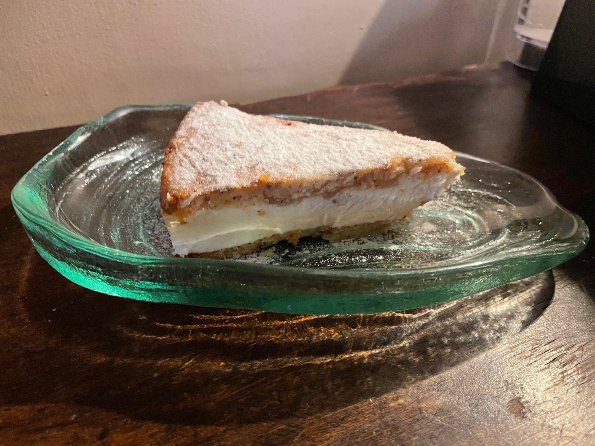 Una rebanada de pastel está en un plato de vidrio sobre una mesa de madera.