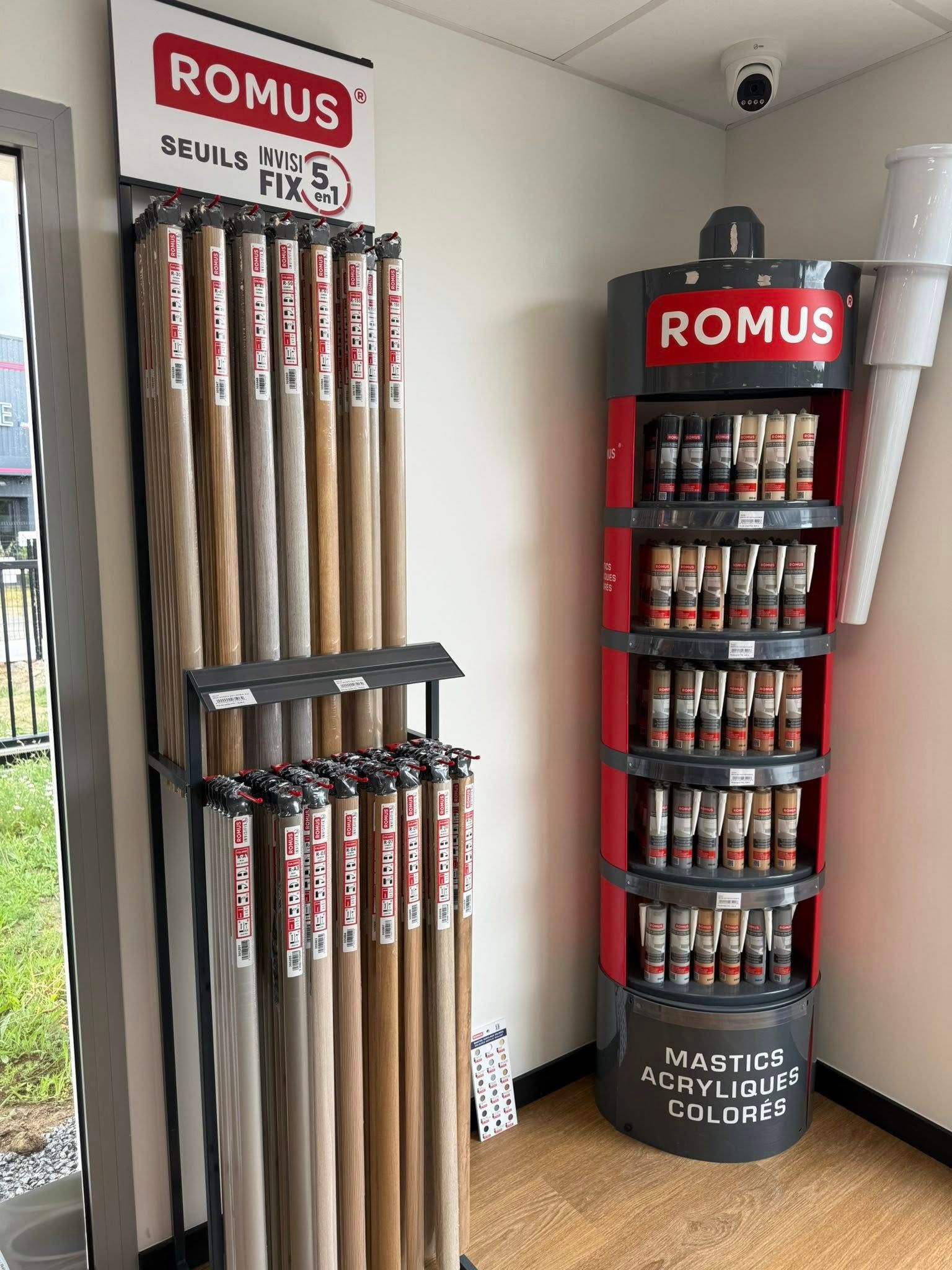 Un présentoir de vente au détail mettant en valeur les barres de transition pour revêtements de sol de la marque ROMUS et des moulures imitation bois.