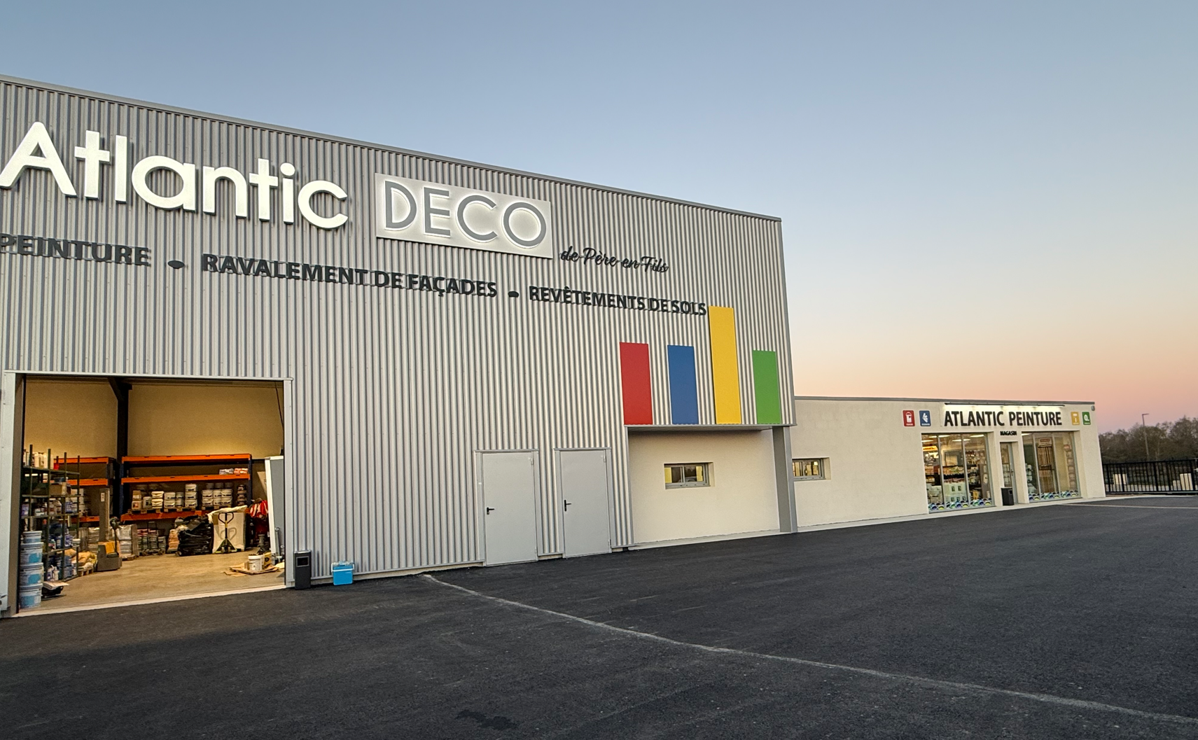 Vue latérale du bâtiment Atlantic Deco avec une grande baie ouverte, un bardage en tôle ondulée grise et un magasin blanc adjacent.