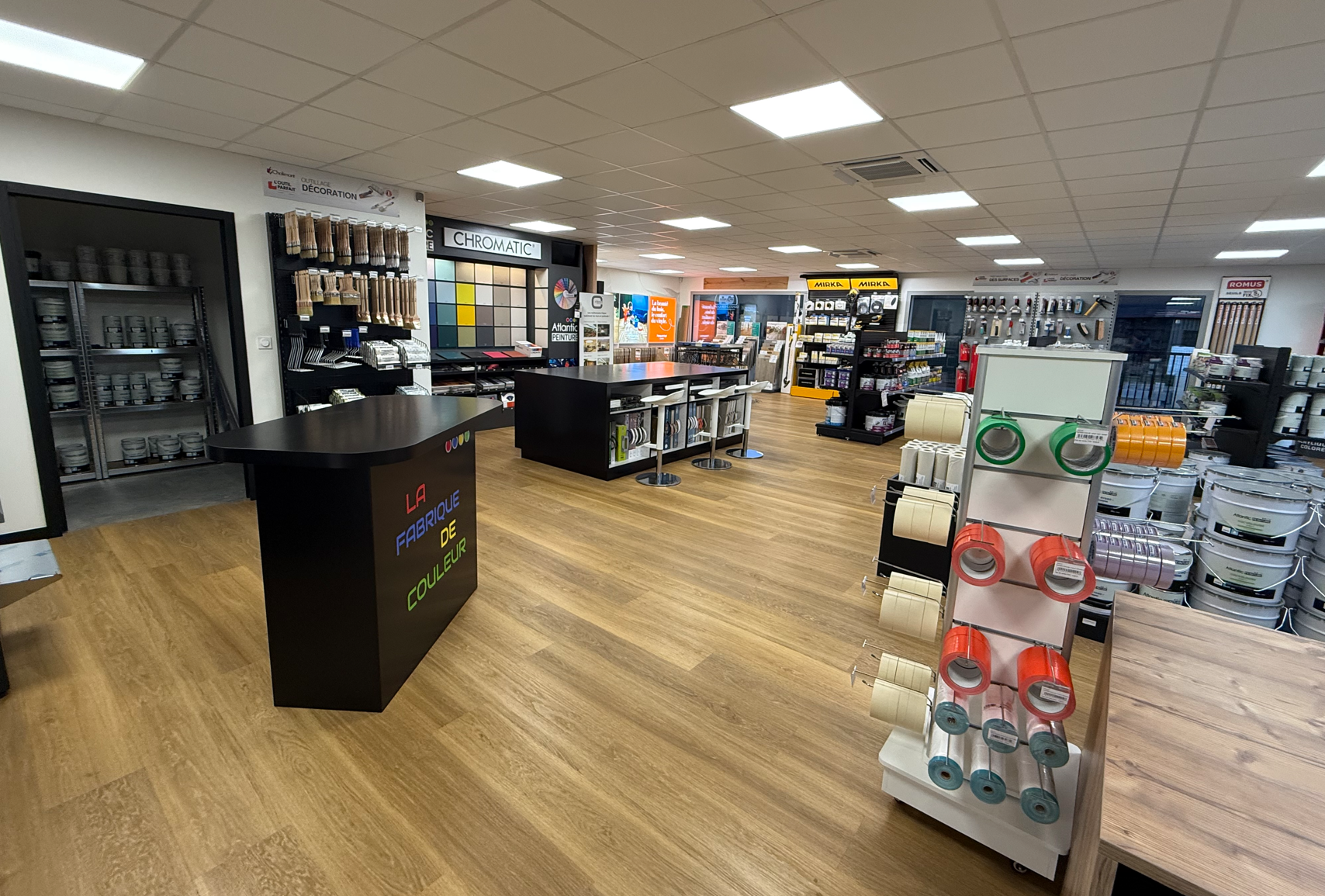 Un intérieur commercial lumineux avec un parquet clair, un comptoir de service central, des étagères et des présentoirs de produits.