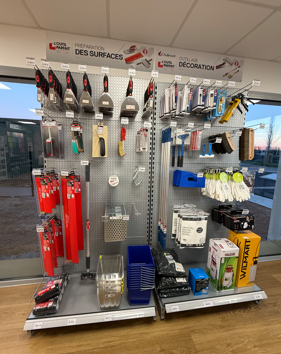 Un présentoir de magasin d'outils de construction et de maçonnerie, comprenant des grattoirs, des truelles, des gants et des fournitures suspendus.