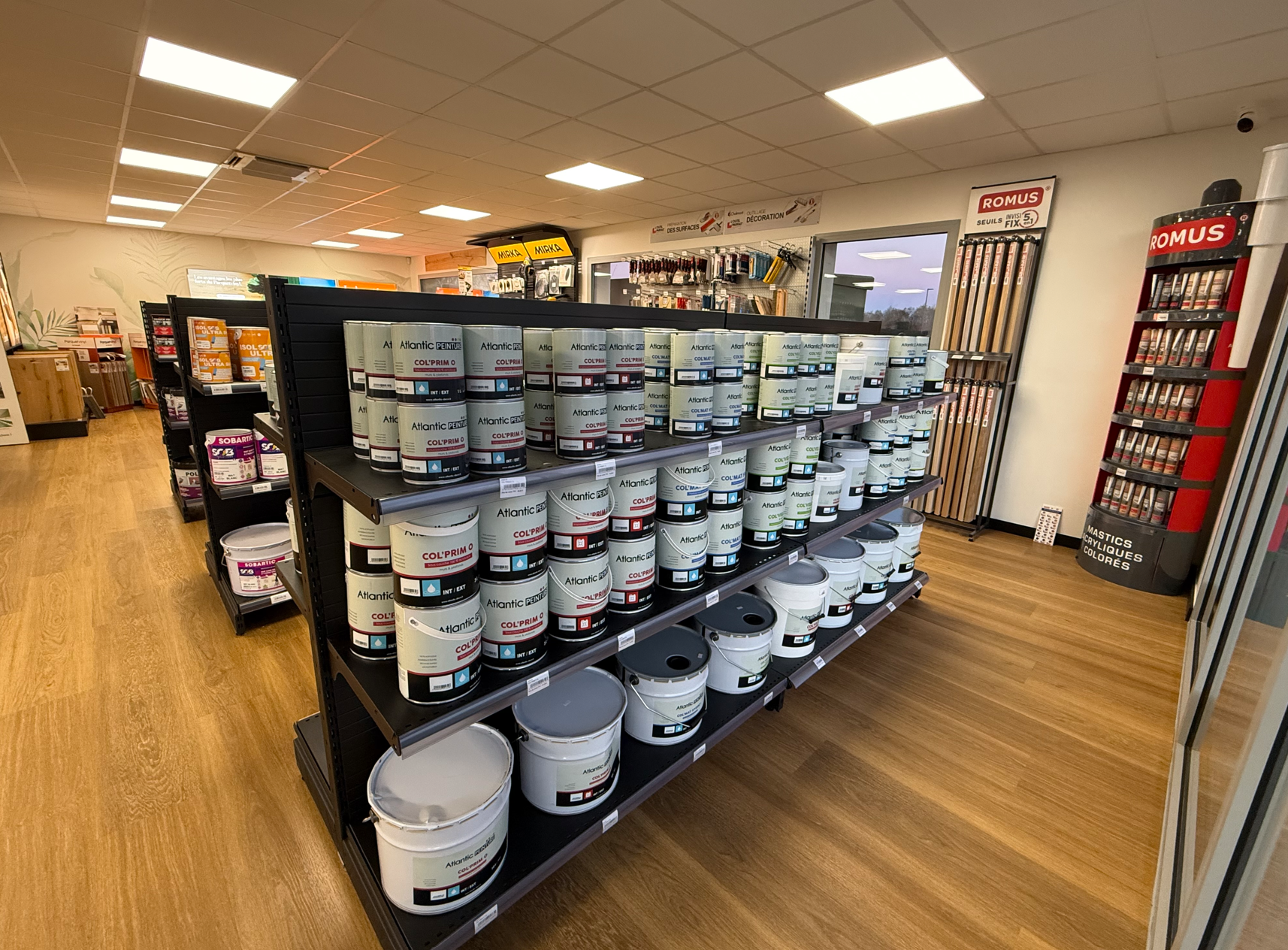 Des étagères remplies de pots de peinture de différentes tailles se trouvent dans un magasin bien éclairé.
