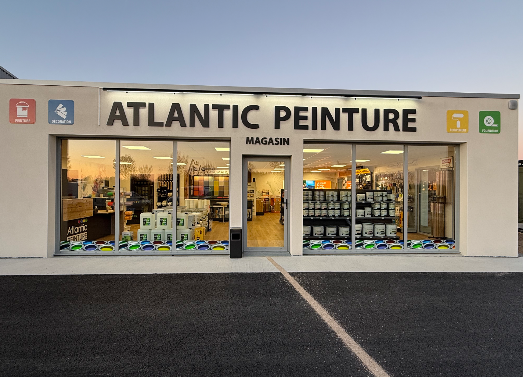 La façade du magasin Atlantic Peinture, un magasin de peinture avec une façade en verre, une enseigne lumineuse et un parking devant.