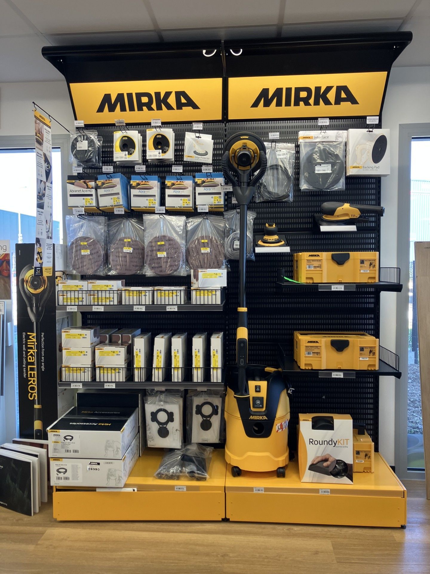 Un présentoir de vente au détail mettant en vedette des outils électriques Mirka jaunes et noirs, du matériel de ponçage et des accessoires.