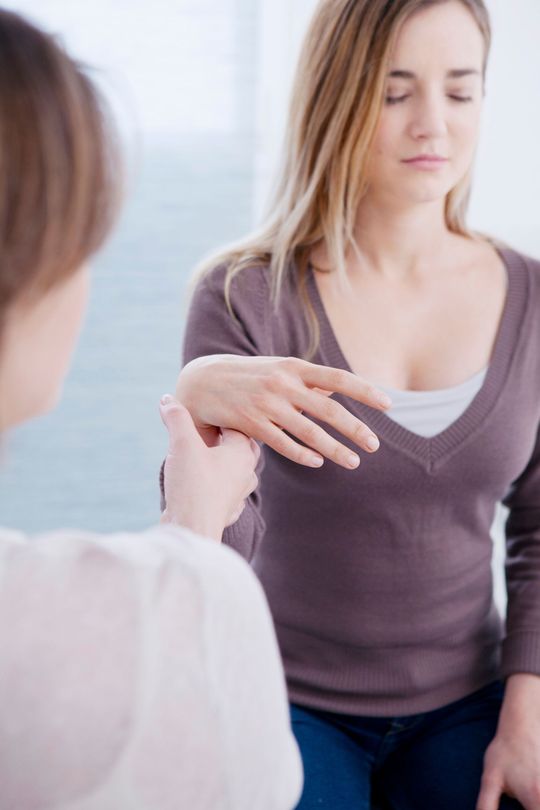 Une jeune femme se fait tenir la main par la thérapeute pour une séance d'hypnose