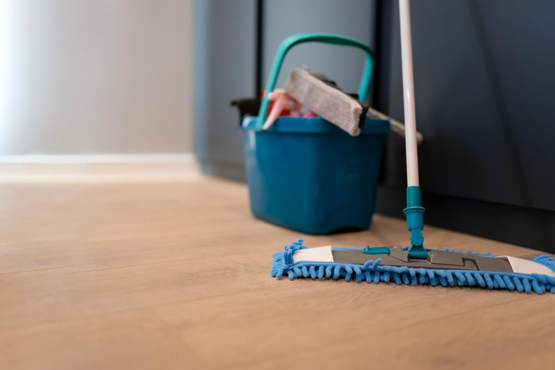 Cubo y fregona azules sobre un suelo de madera en el interior de una vivienda.
