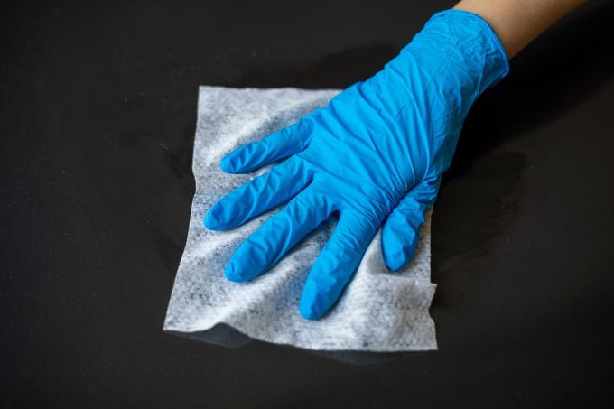 Una mano enguantada de azul limpia una superficie negra con un paño blanco.