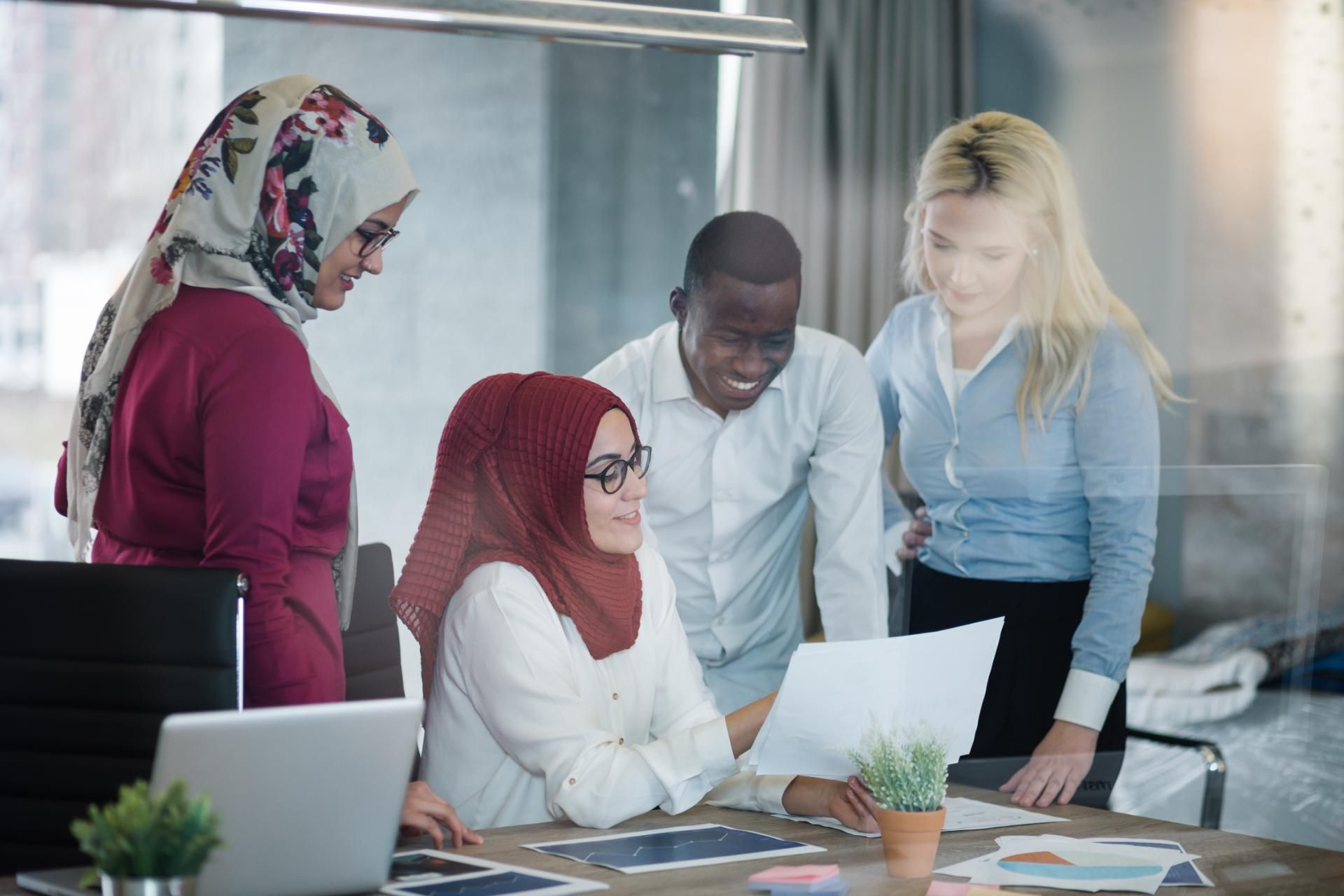 Vier Menschen unterschiedlicher Nationen beugen sich über einen Laptop