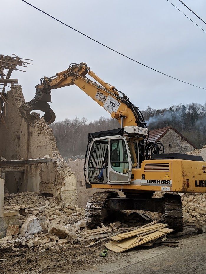 Pelleteuse avec pince en train de détruire un mur en pierre